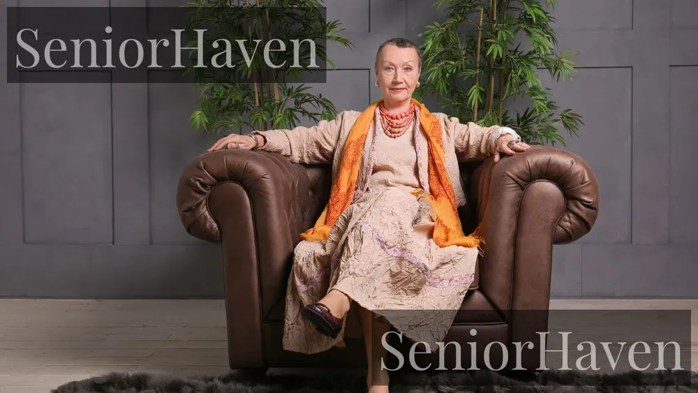 A mature woman seated in a large armchair with her legs crossed and one foot dangling